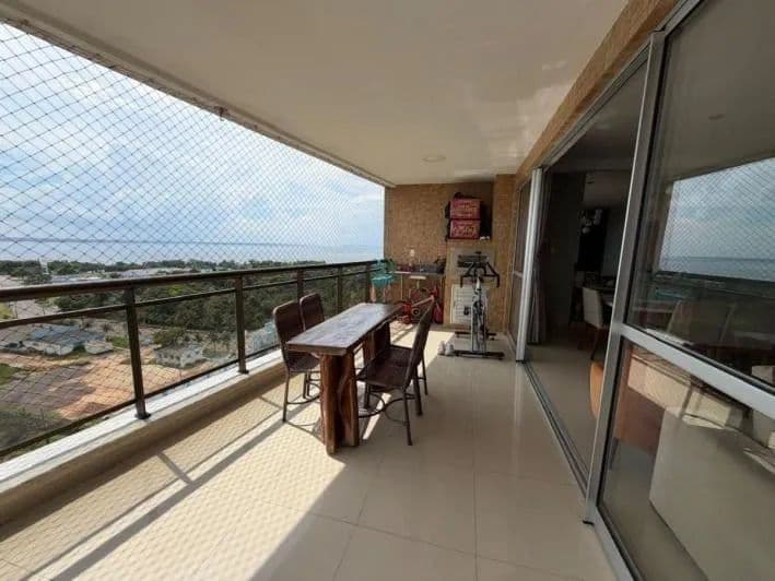 Varanda com mesa de madeira, cadeiras, churrasqueira e vista aberta para o rio.